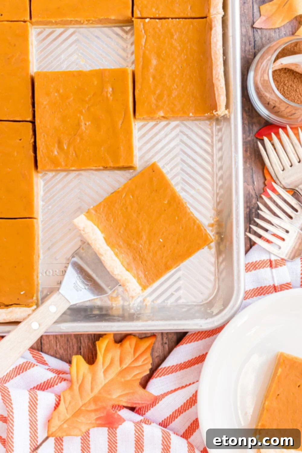 Effortless 4-Ingredient Sheet Pan Pumpkin Pie 15 rustic wooden table with a metal sheet pan with slices of pumpkin pie in it, with a spatula lifting up more slices of pie on table