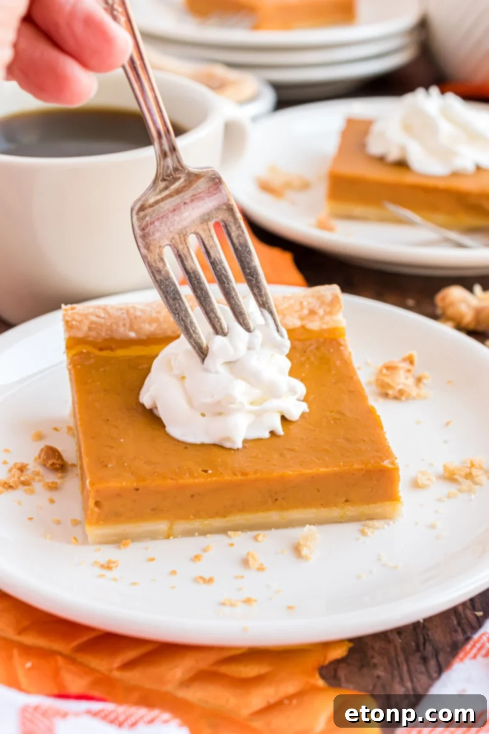 Effortless 4-Ingredient Sheet Pan Pumpkin Pie 16 wooden table with a few white plates with slices of pumpkin pie topped with whipped cream. One plate has a fork poking into the whipped cream on top of the pie