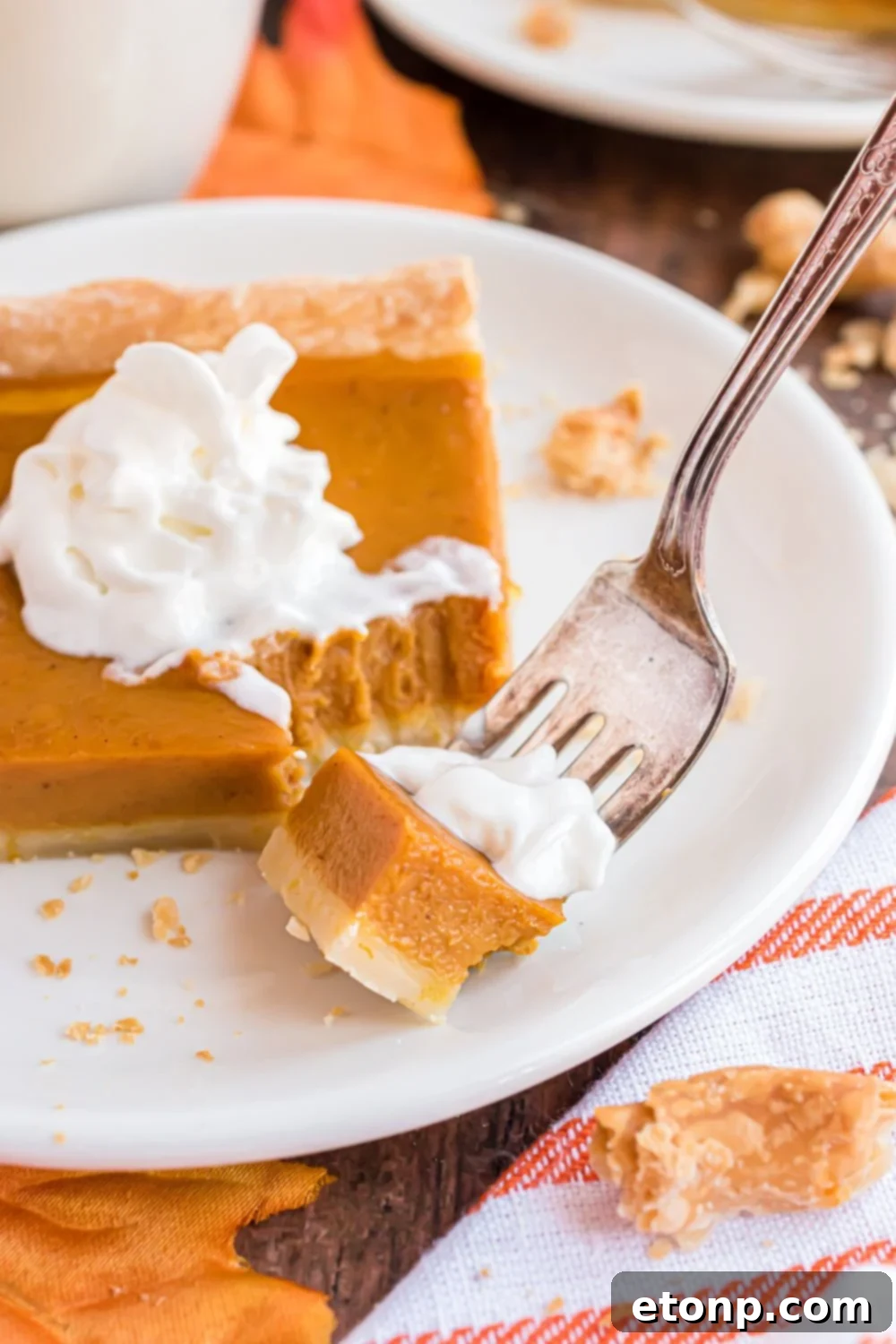 Effortless 4-Ingredient Sheet Pan Pumpkin Pie 20 slice of Sheet Pan Pumpkin Pie on a white plate with a fork with a biteful on it. Then a towel to side on a wooden table