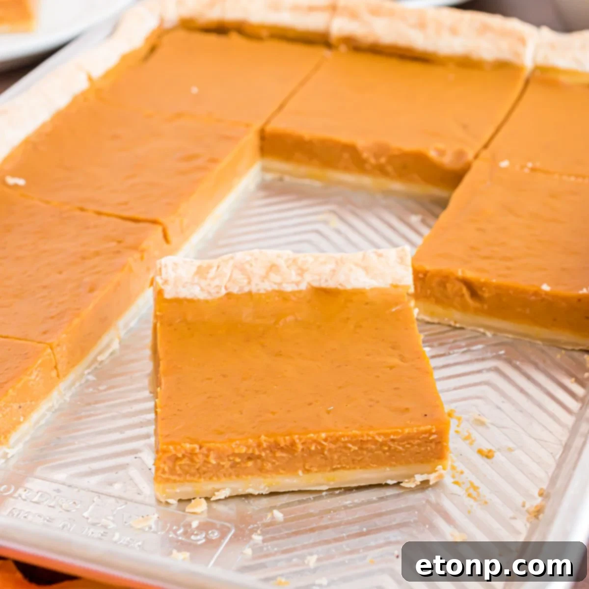 Effortless 4-Ingredient Sheet Pan Pumpkin Pie 3 metal sheet pan sitting on table with a few slices of the pie gone to show how many slices of pie you get out of this slab pie recipe