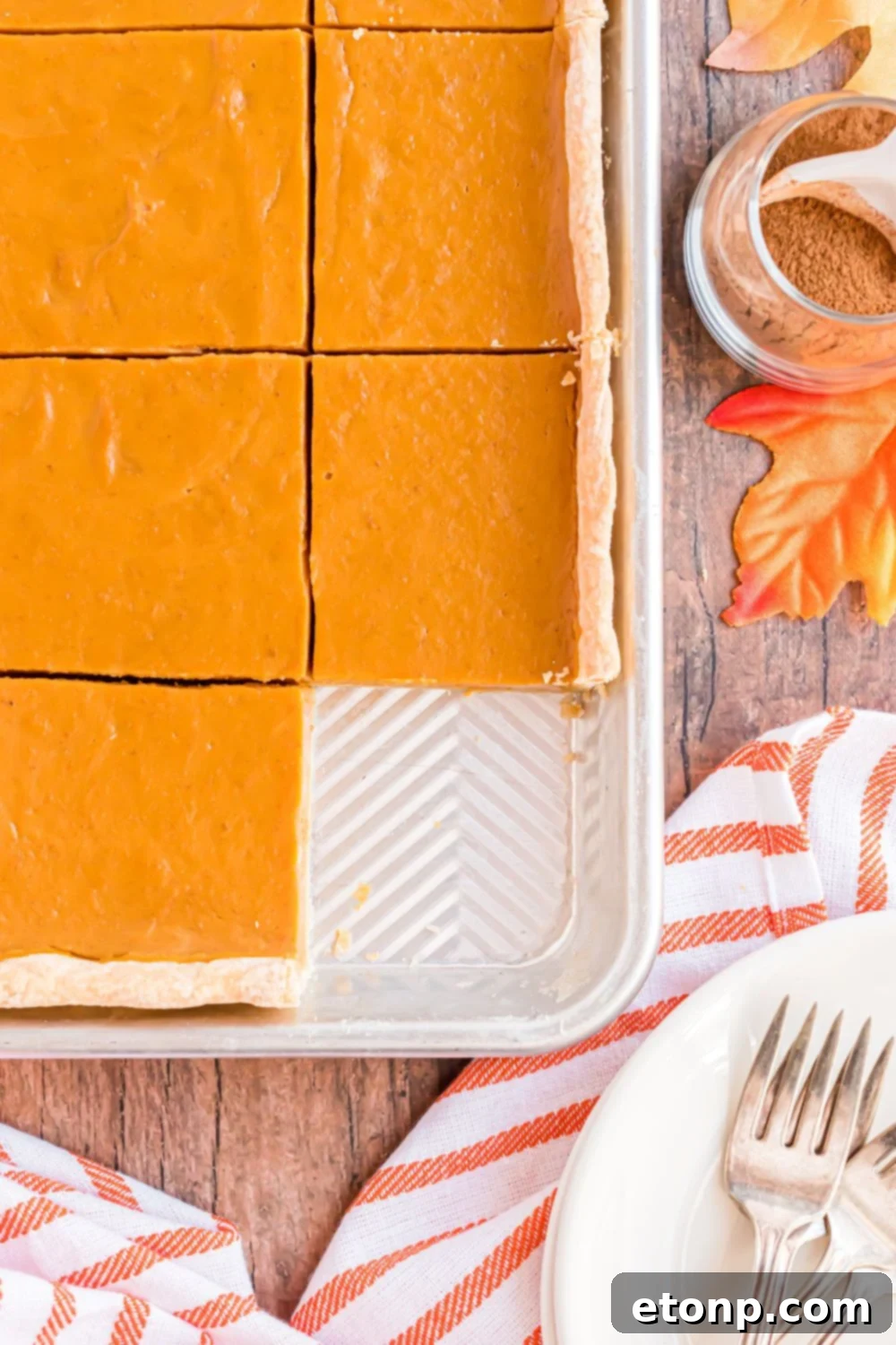Effortless 4-Ingredient Sheet Pan Pumpkin Pie 21 rustic wooden table with fall decorations and a Sheet Pan Pumpkin Pie with one slice removed from the pan, with a white plate and fork sitting in front of the sheet pan.