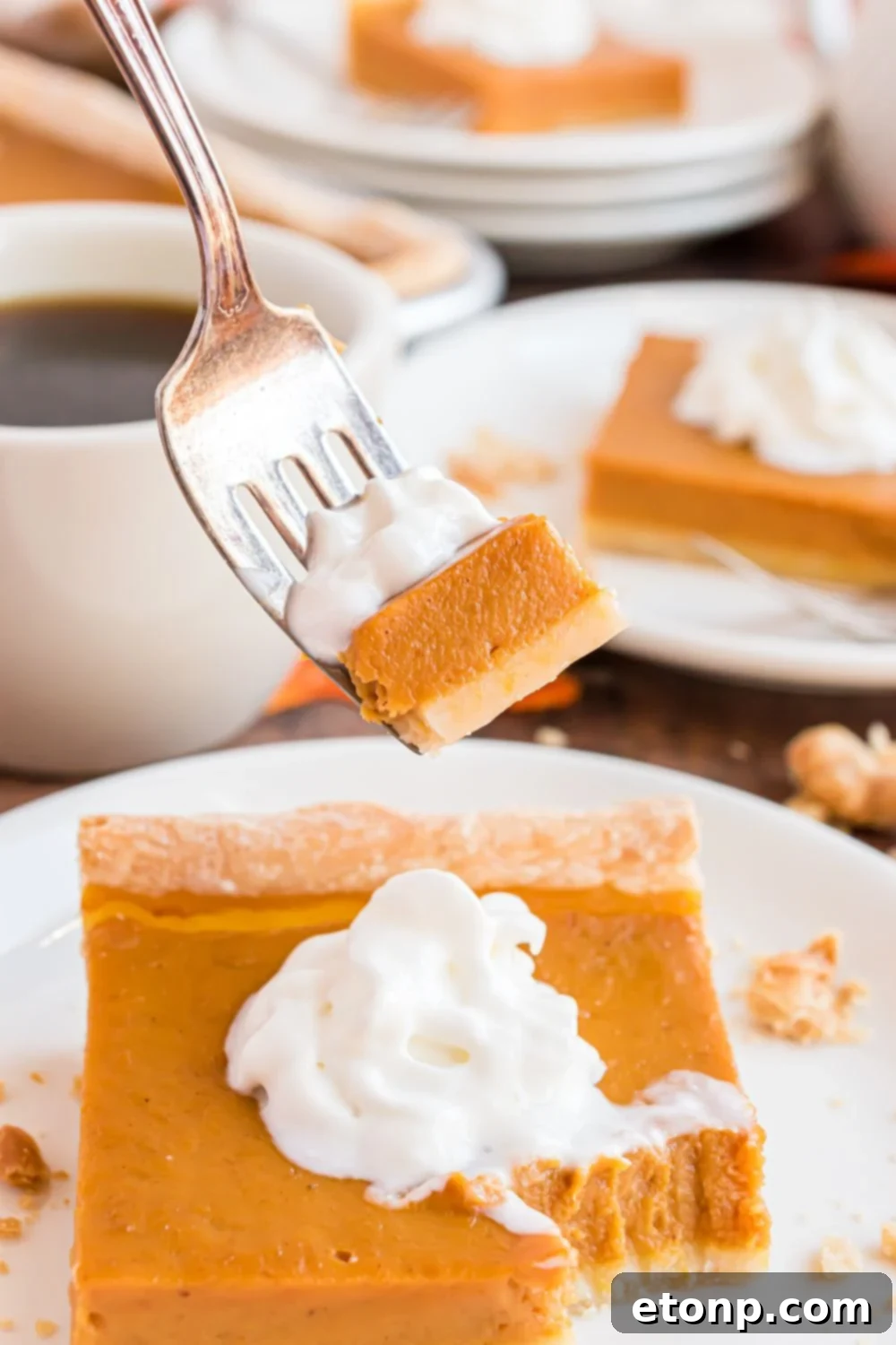 Effortless 4-Ingredient Sheet Pan Pumpkin Pie 22 a handful of plates spread out on a wooden table with pumpkin pie topped with whipped cream and coffee cup in the center of table. Then one slice of pie has a fork with some of the pie and whipped cream on the fork.