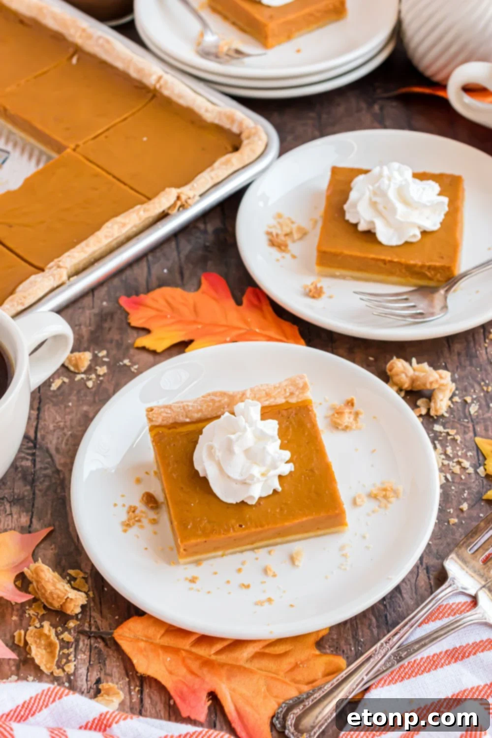 Effortless 4-Ingredient Sheet Pan Pumpkin Pie 5 wooden table decorated for the fall season with white plates topped with slices of pumpkin pie topped with whipped cream. Then to side you have a metal sheet pan full of more sheet pan pumpkin pie
