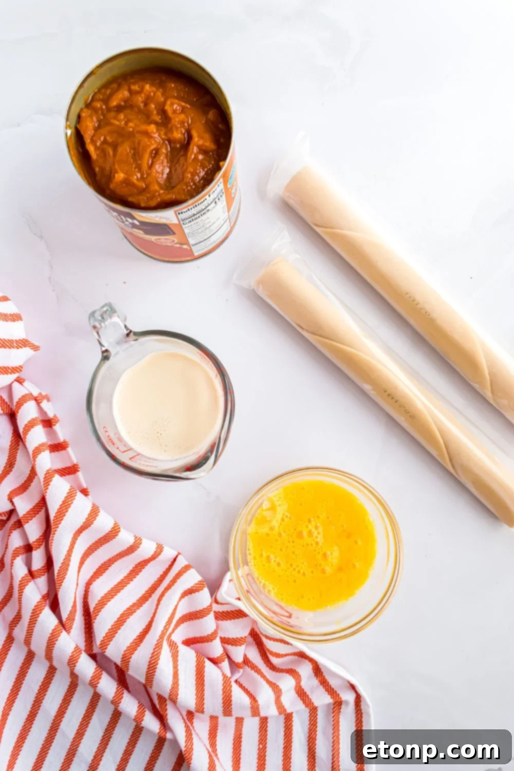 Effortless 4-Ingredient Sheet Pan Pumpkin Pie 6 Sheet Pan Pumpkin Pie ingredients on a marble counter. A can of pumpkin puree, two rolls of pie crust, a bowl of egg mixture, and evaporated milk in a measuring cup