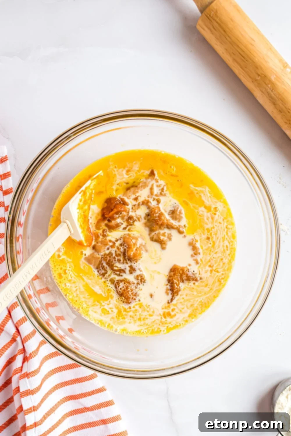 Effortless 4-Ingredient Sheet Pan Pumpkin Pie 8 glass bowl full of all the ingredients for making pumpkin pie filling, with a rolling pin to side on the white table
