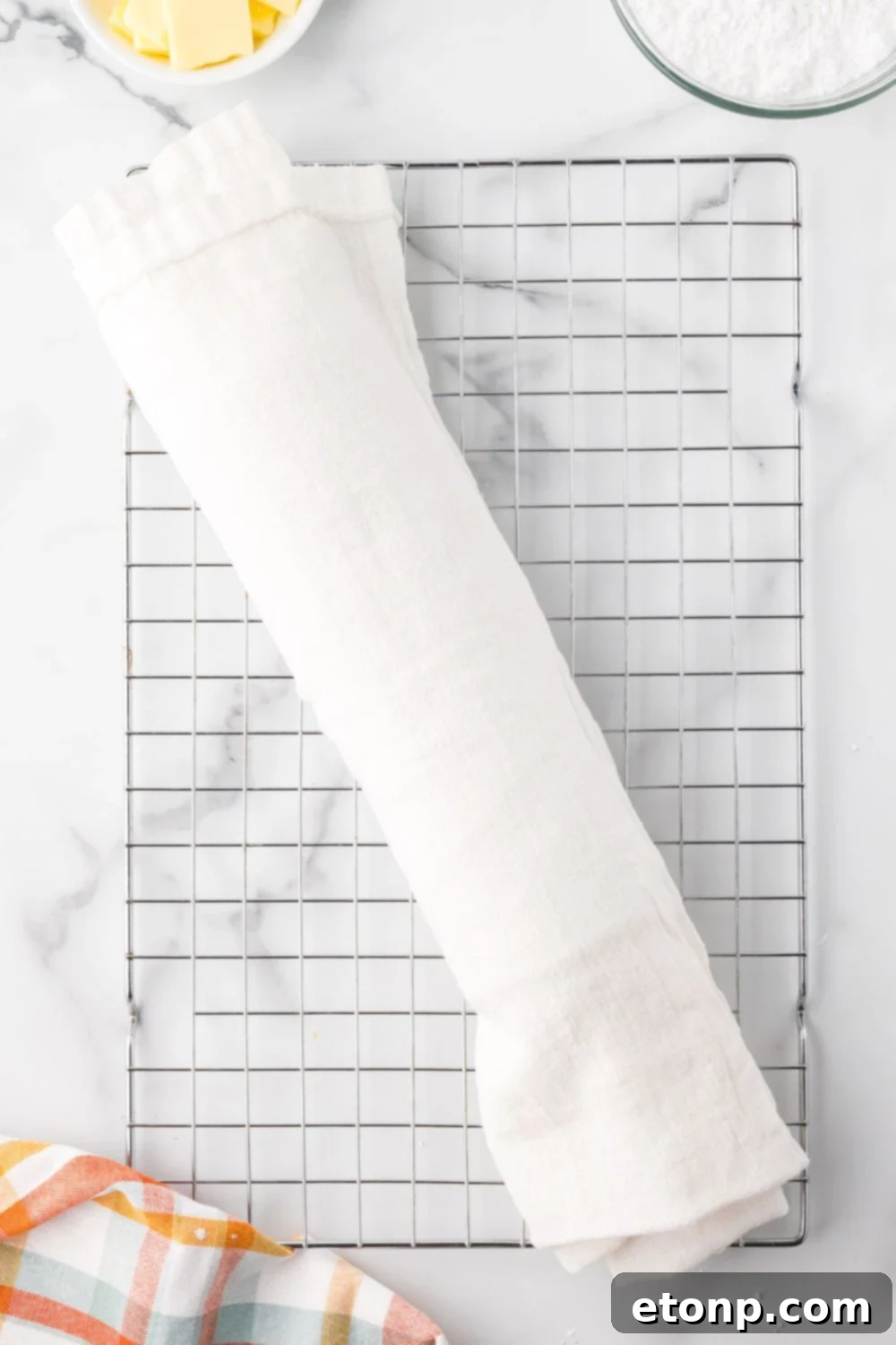 Pumpkin Cake Roll wrapped up in a white towel on a cooling rack on a marble counter