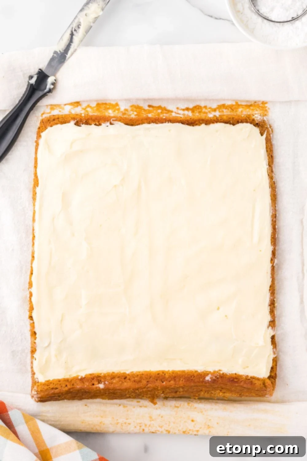 pumpkin roll laid out on marble counter spread with cream cheese filling all over