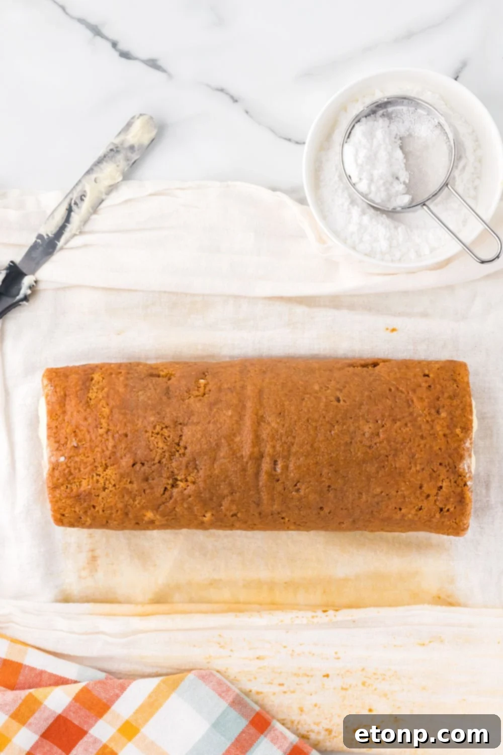 Pumpkin Cake Roll being rolled up with parchment paper under the pumpkin cake