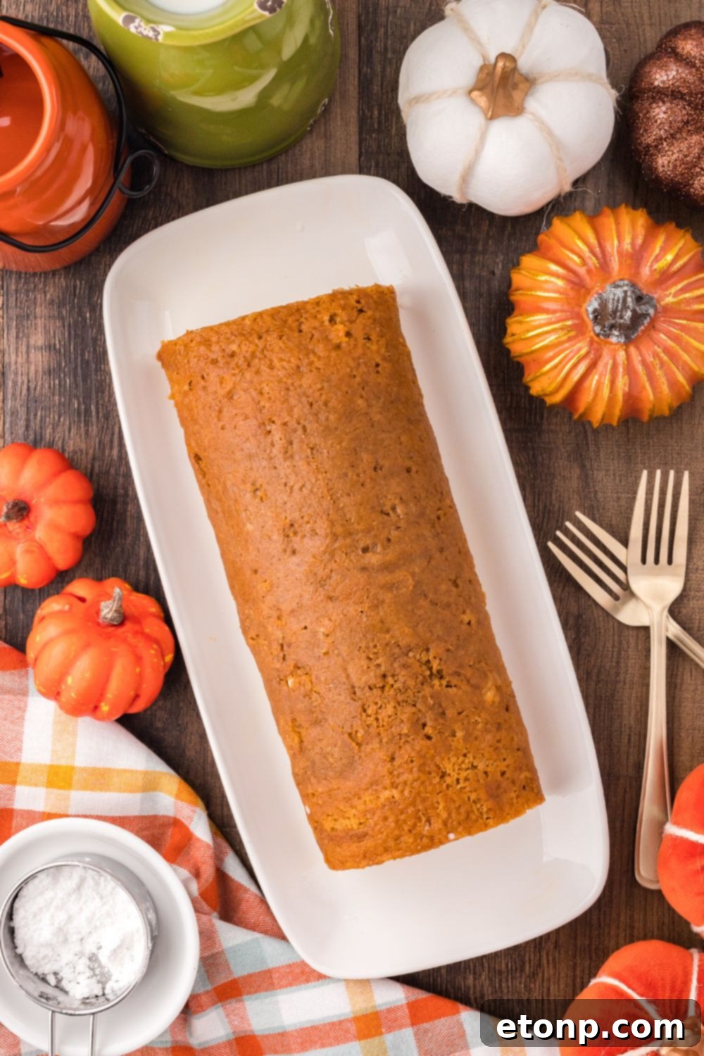 Pumpkin Cake Roll sitting on a long platter with faux pumpkins to side and forks on side