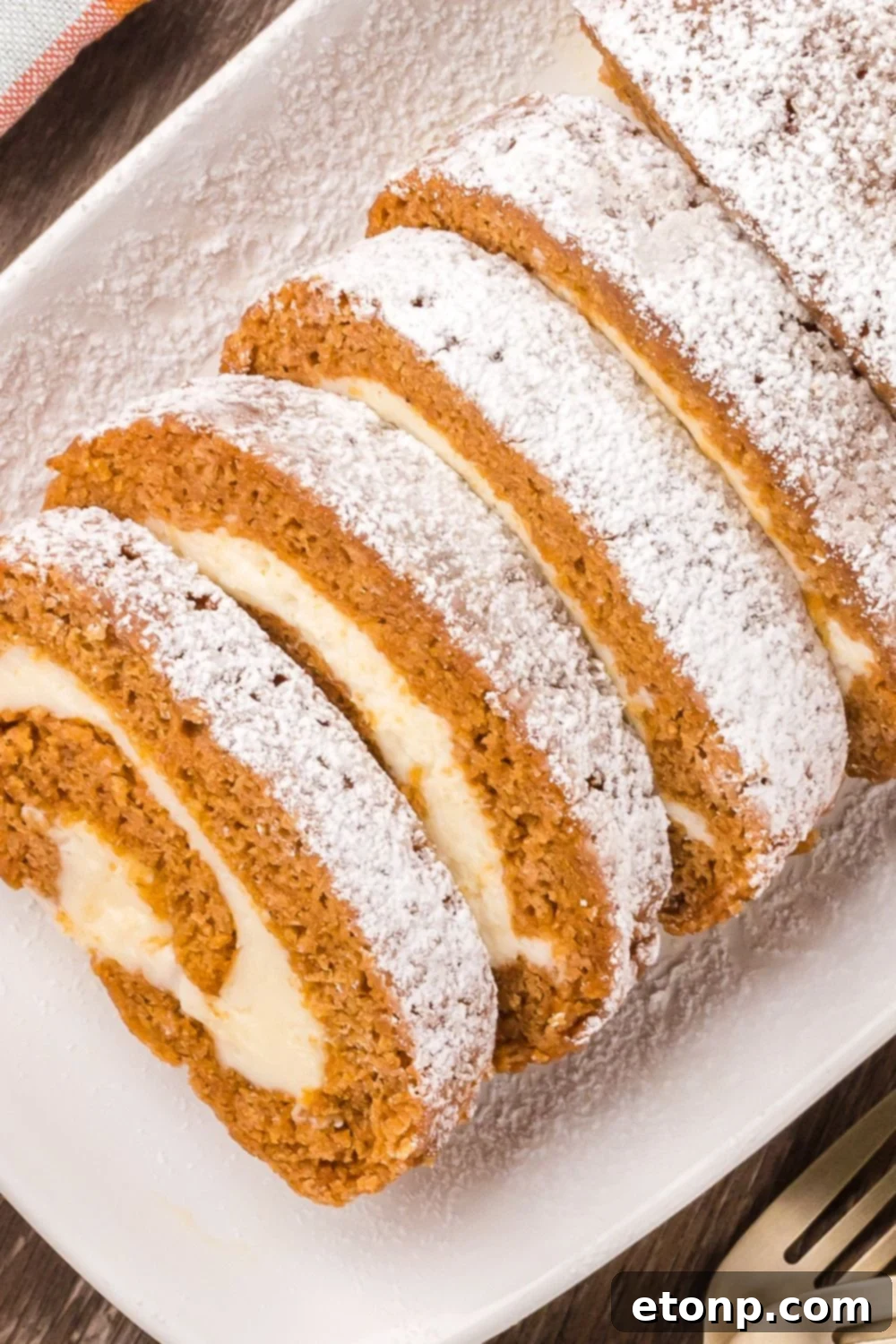 sliced Pumpkin Cake Roll on a tray sitting on a wooden table with a fork to the side