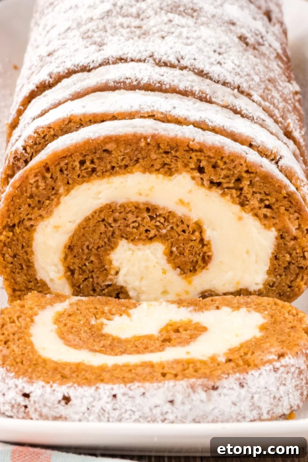 close up of Pumpkin Cake Roll on a platter so you can see the swirl of filling in the pumpkin roll