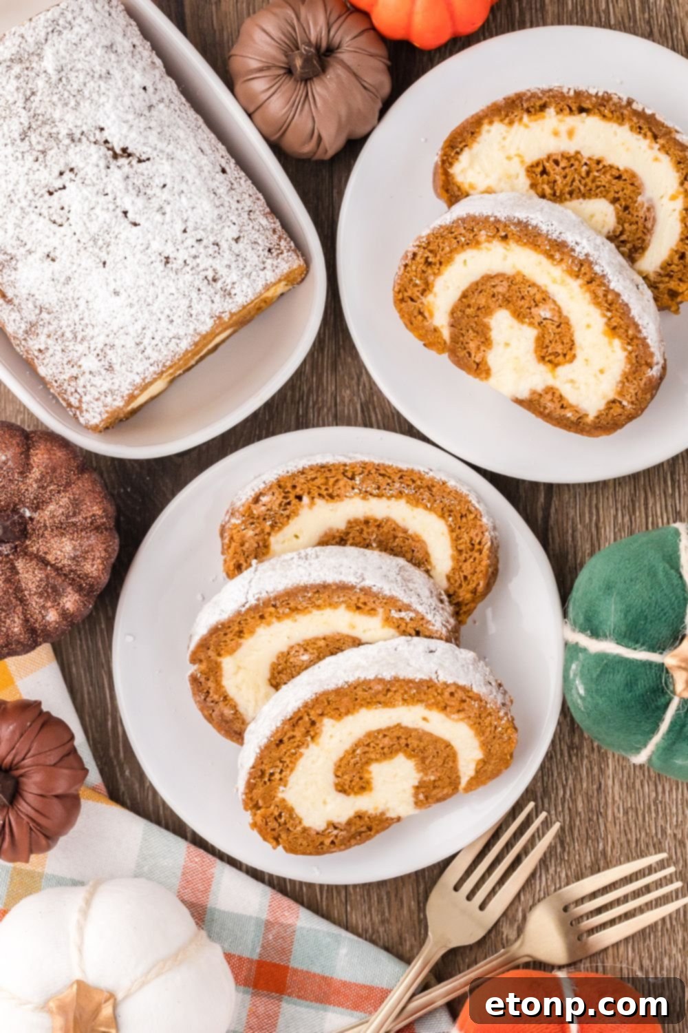 fall rustic wooden table with faux pumpkins and plates with slices of Pumpkin Cake Roll on it, and a platter to the back with more of the pumpkin cake on it