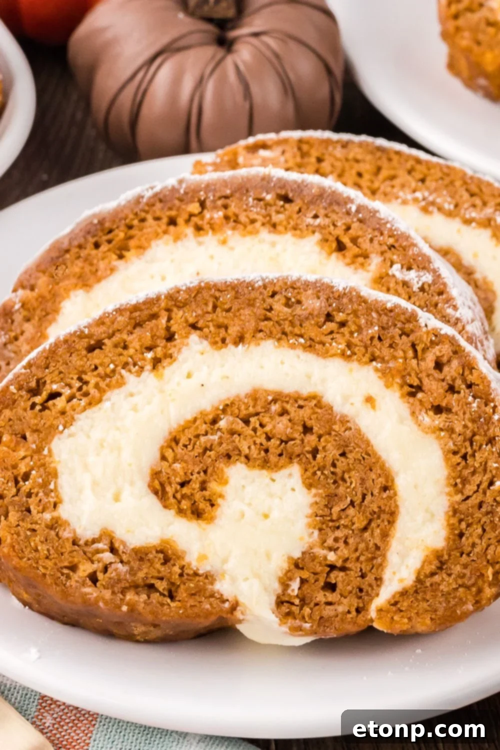 a white plate on table with three thick slices of Pumpkin Cake Roll on it, and mini pumpkins to side of plate