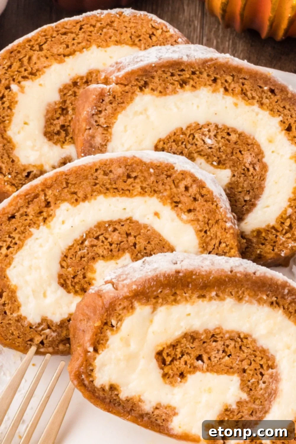 thick slices of Pumpkin Cake Roll on a white plate with a fork sitting in front of the plate that is sitting on a wooden table