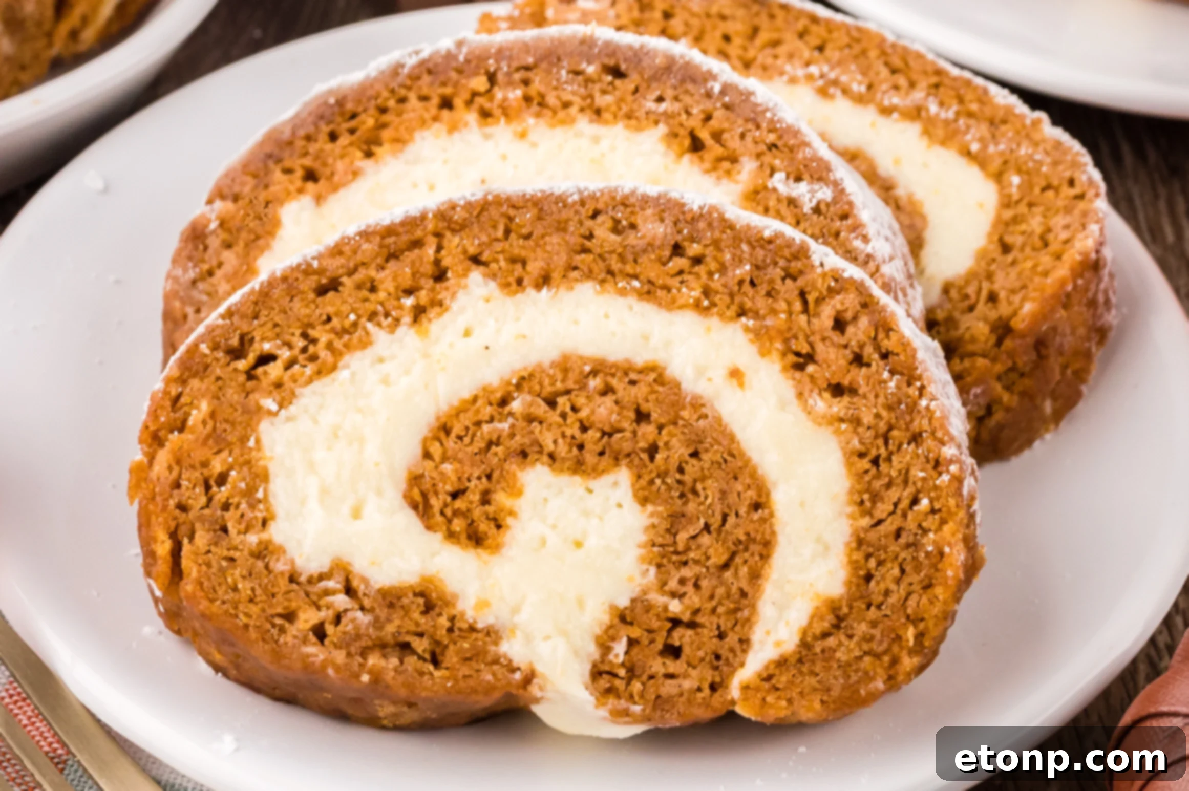 Pumpkin Cake Roll sliced on white plates placed on table with a few faux pumpkins around