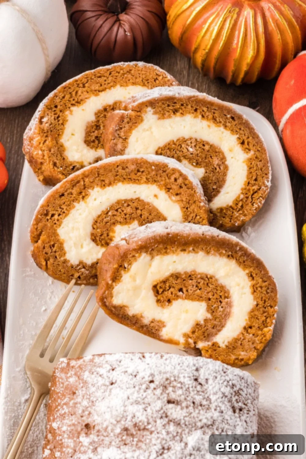 Pumpkin Cake Roll sliced and placed on a platter, and faux pumpkins around the platter for a fall themed rustic look