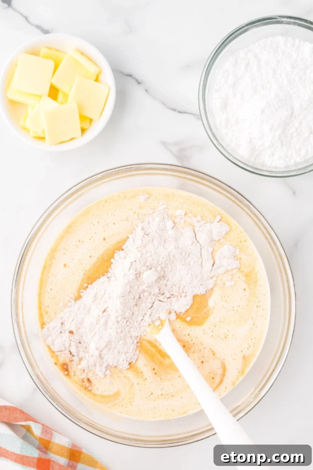 mixing up Pumpkin Cake Roll batter in a glass bowl on marble counter with butter and powdered sugar in smaller bowls to the side