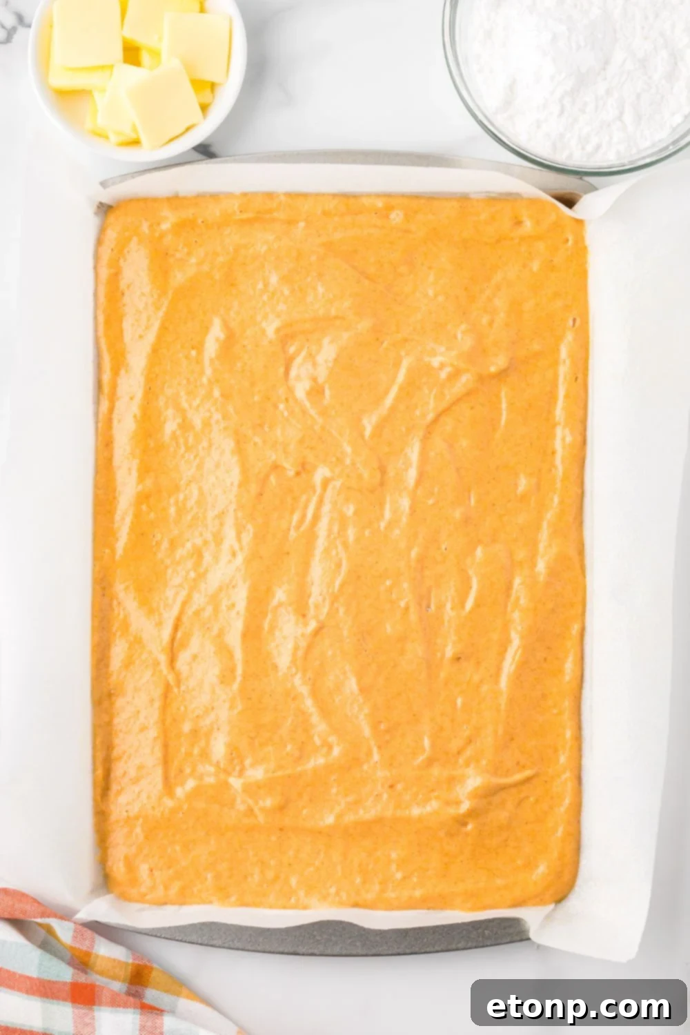 Pumpkin Cake Roll batter spread out in a baking pan sitting on table with parchment paper under it