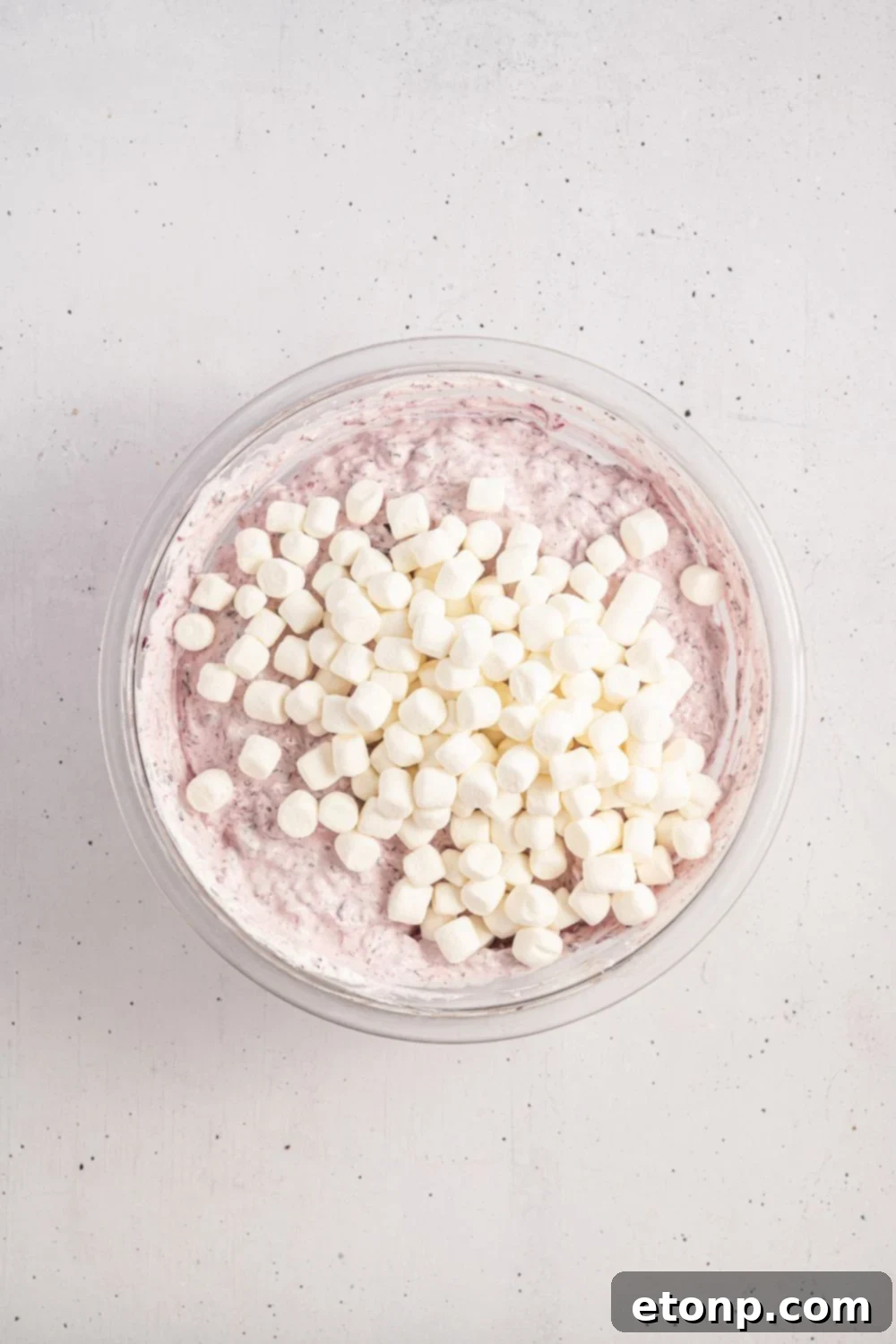 marshmallows on top of cranberry salad being assembled in the glass bowl 
