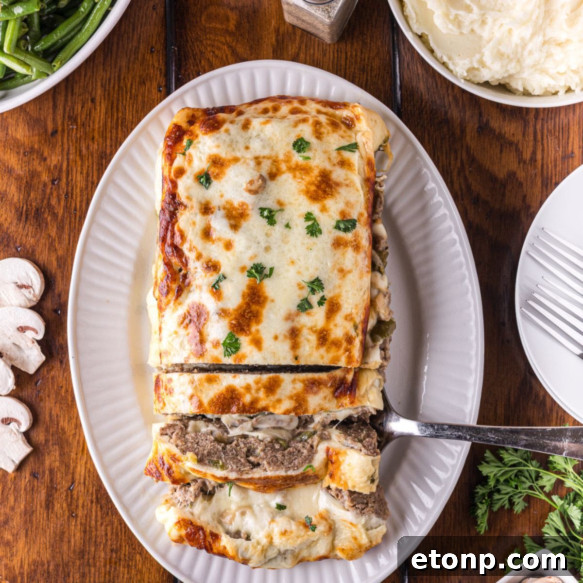 Cheesy Philly Stuffed Meatloaf with Peppers and Onions 2 Stuffed Philly Cheesesteak Meatloaf on a white platter on wooden table that is partly sliced and ready to serve