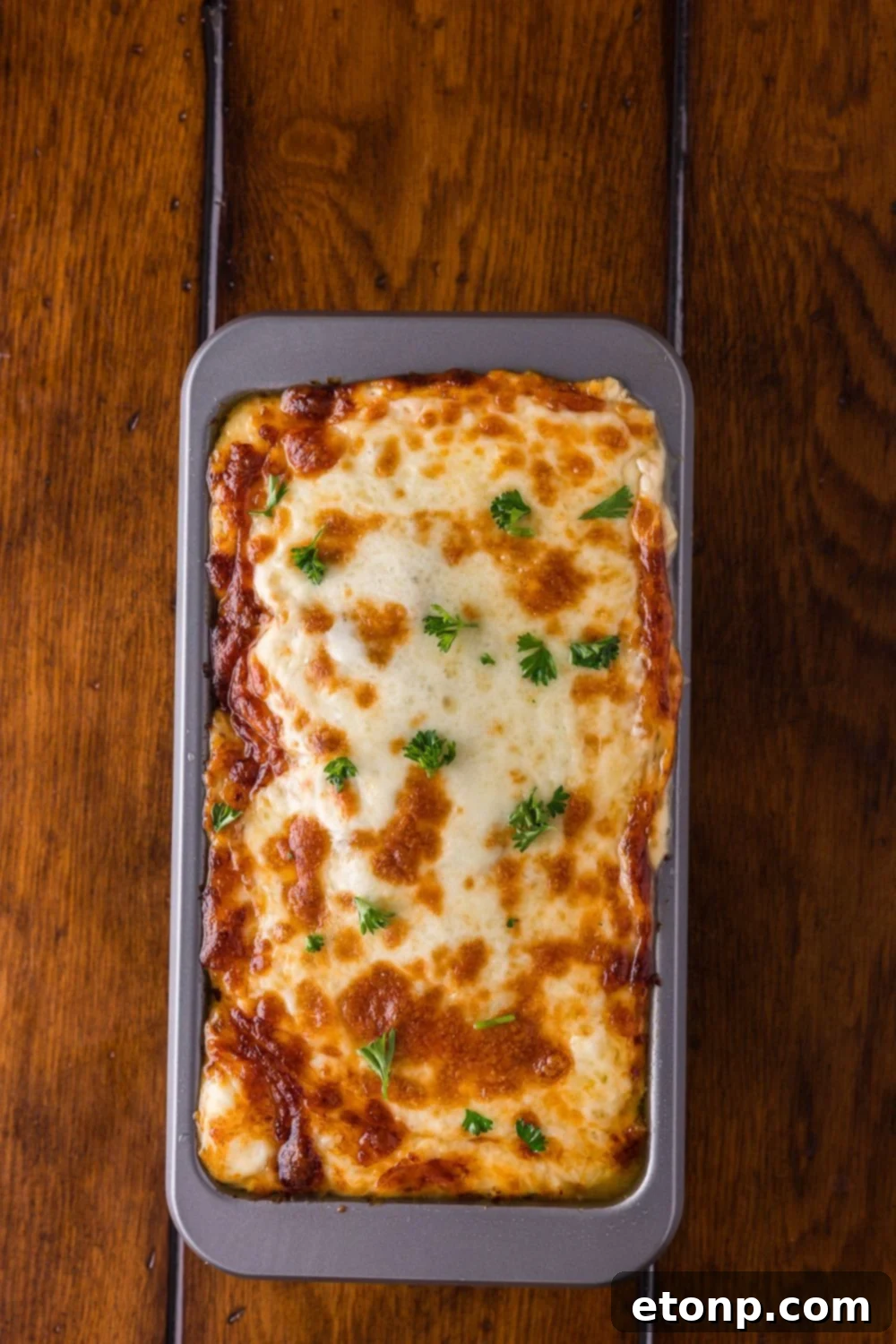 Cheesy Philly Stuffed Meatloaf with Peppers and Onions 11 Stuffed Philly Cheesesteak Meatloaf baked and sitting in a loaf pan on wooden table