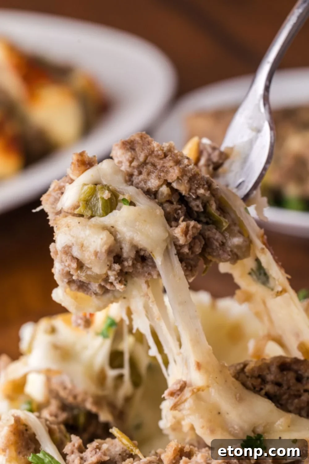 Cheesy Philly Stuffed Meatloaf with Peppers and Onions 12 fork with a bunch of cheesy Stuffed Philly Cheesesteak Meatloaf being lifted up off a plate full of more meatloaf sitting on wooden table