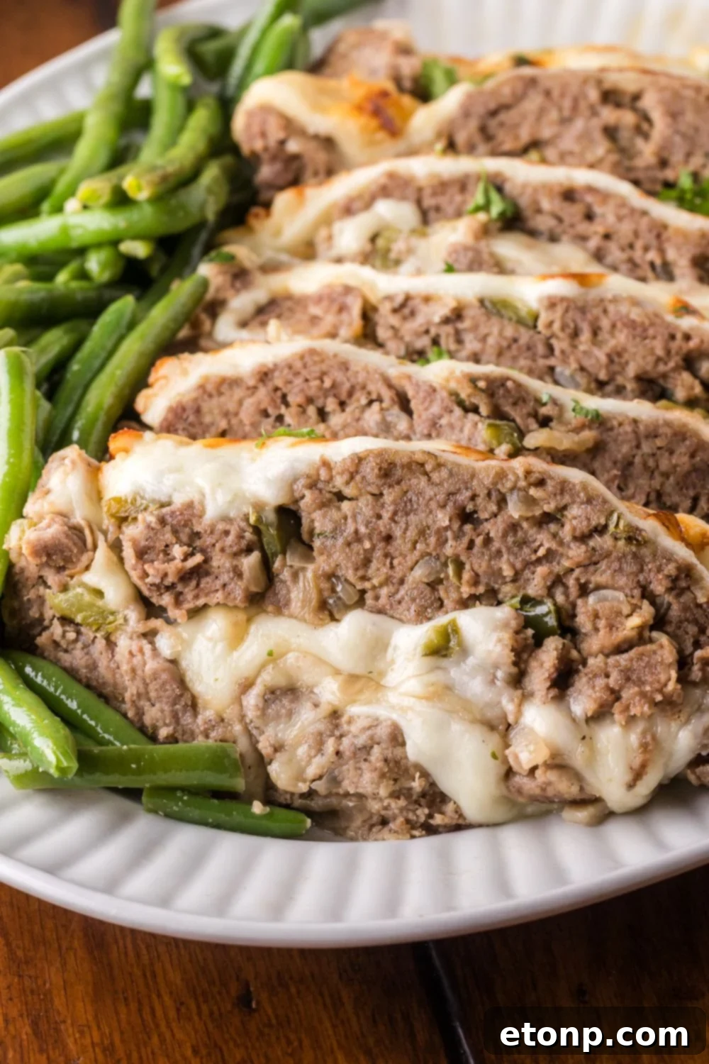 Cheesy Philly Stuffed Meatloaf with Peppers and Onions 13 platter with greens on it, and then topped with sliced Stuffed Philly Cheesesteak Meatloaf