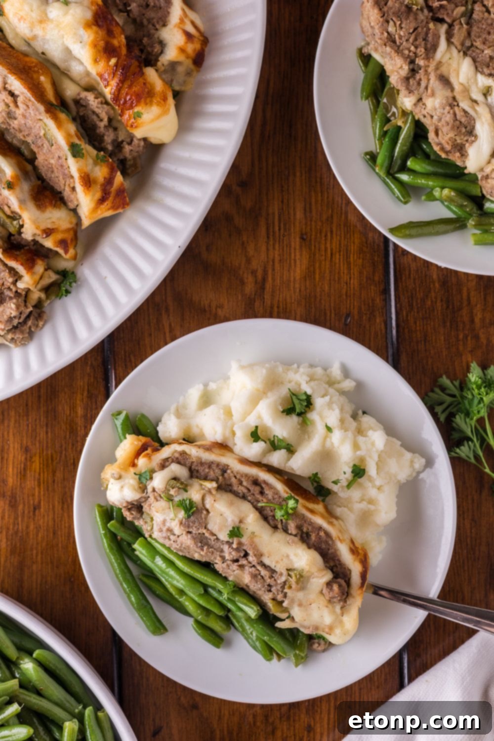 Cheesy Philly Stuffed Meatloaf with Peppers and Onions 18 a dinner table with a platter full of sliced Stuffed Philly Cheesesteak Meatloaf, and plates that have meatloaf, mashed potatoes and green beans on it