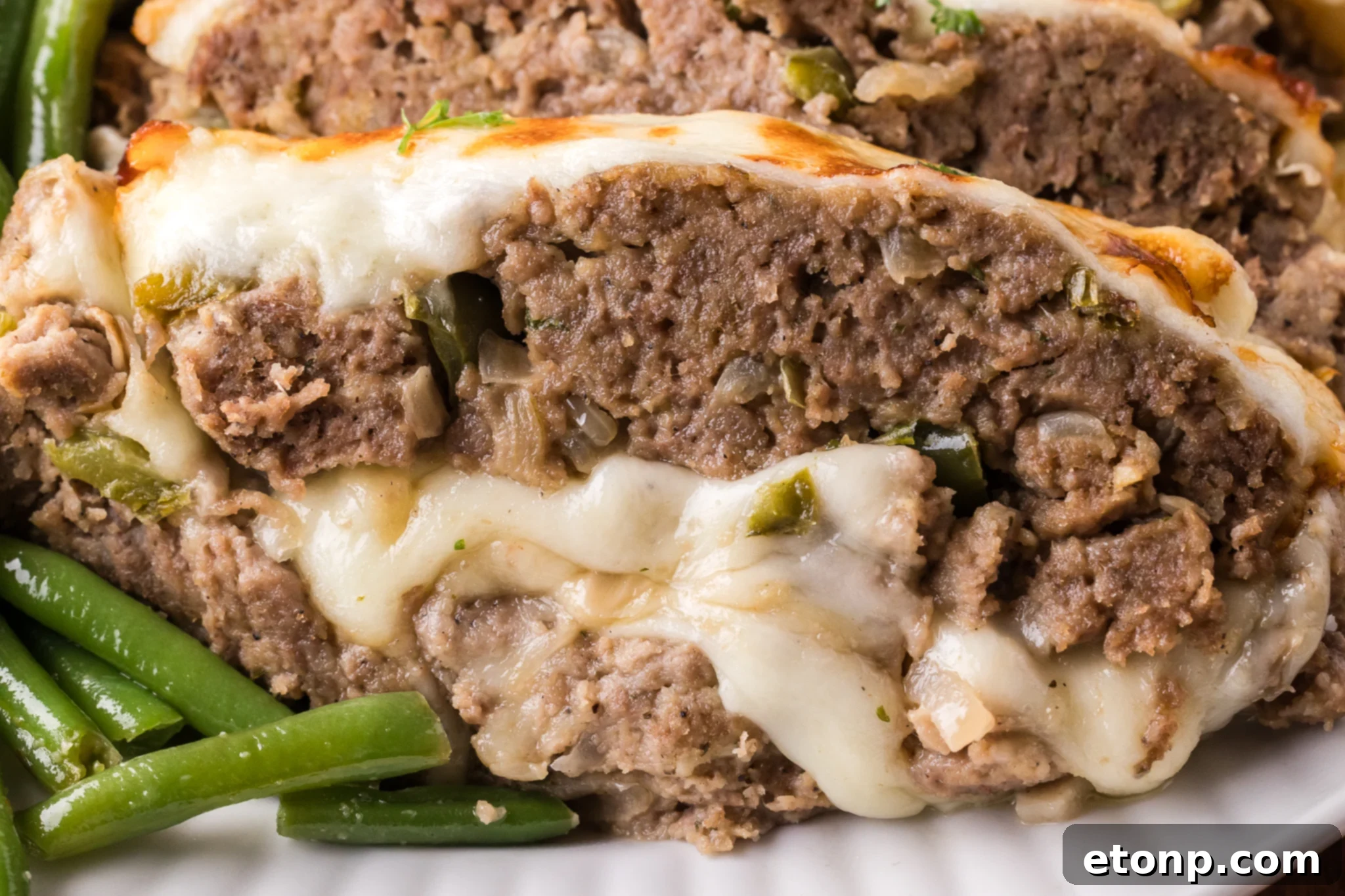 Cheesy Philly Stuffed Meatloaf with Peppers and Onions 20 Up close shot of the cheesy inside of the Philly Cheesesteak Meatloaf sliced on a white serving plate