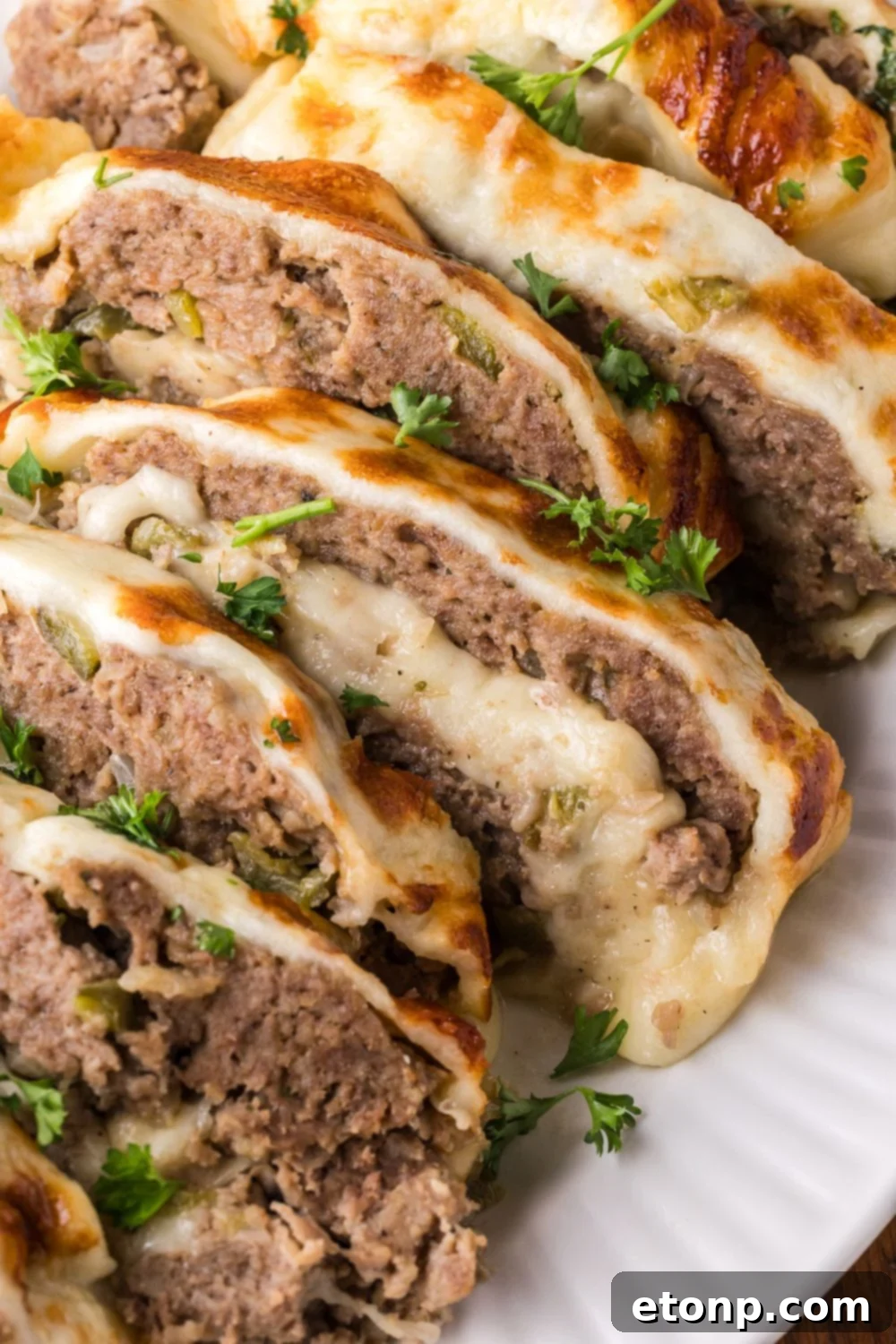 Cheesy Philly Stuffed Meatloaf with Peppers and Onions 3 sliced Stuffed Philly Cheesesteak Meatloaf on a white platter that is sprinkled with parsley on top of meatloaf