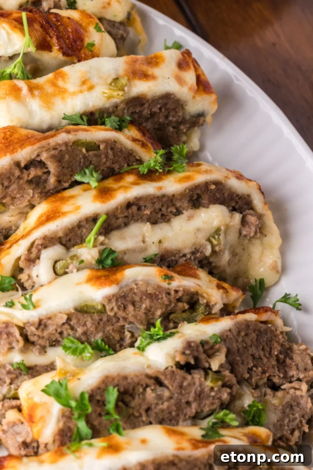 Cheesy Philly Stuffed Meatloaf with Peppers and Onions 21 a white plate on wooden table with sliced Stuffed Philly Cheesesteak Meatloaf on plate topped with chopped parsley