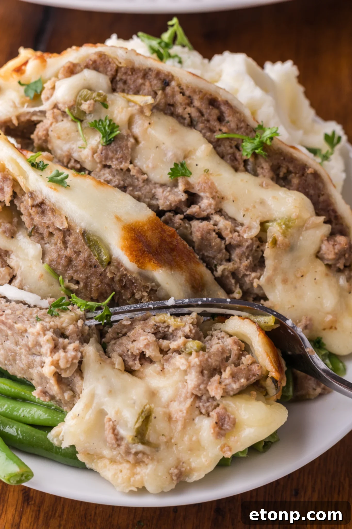 Cheesy Philly Stuffed Meatloaf with Peppers and Onions 22 Up close shot of the Philly Cheesesteak Meatloaf sliced on a white serving plate with a fork taking out a bite