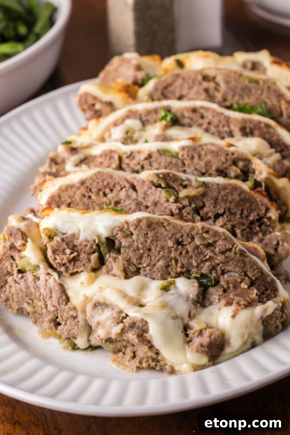 Cheesy Philly Stuffed Meatloaf with Peppers and Onions 23 wooden table with a plate full of sliced Stuffed Philly Cheesesteak Meatloaf