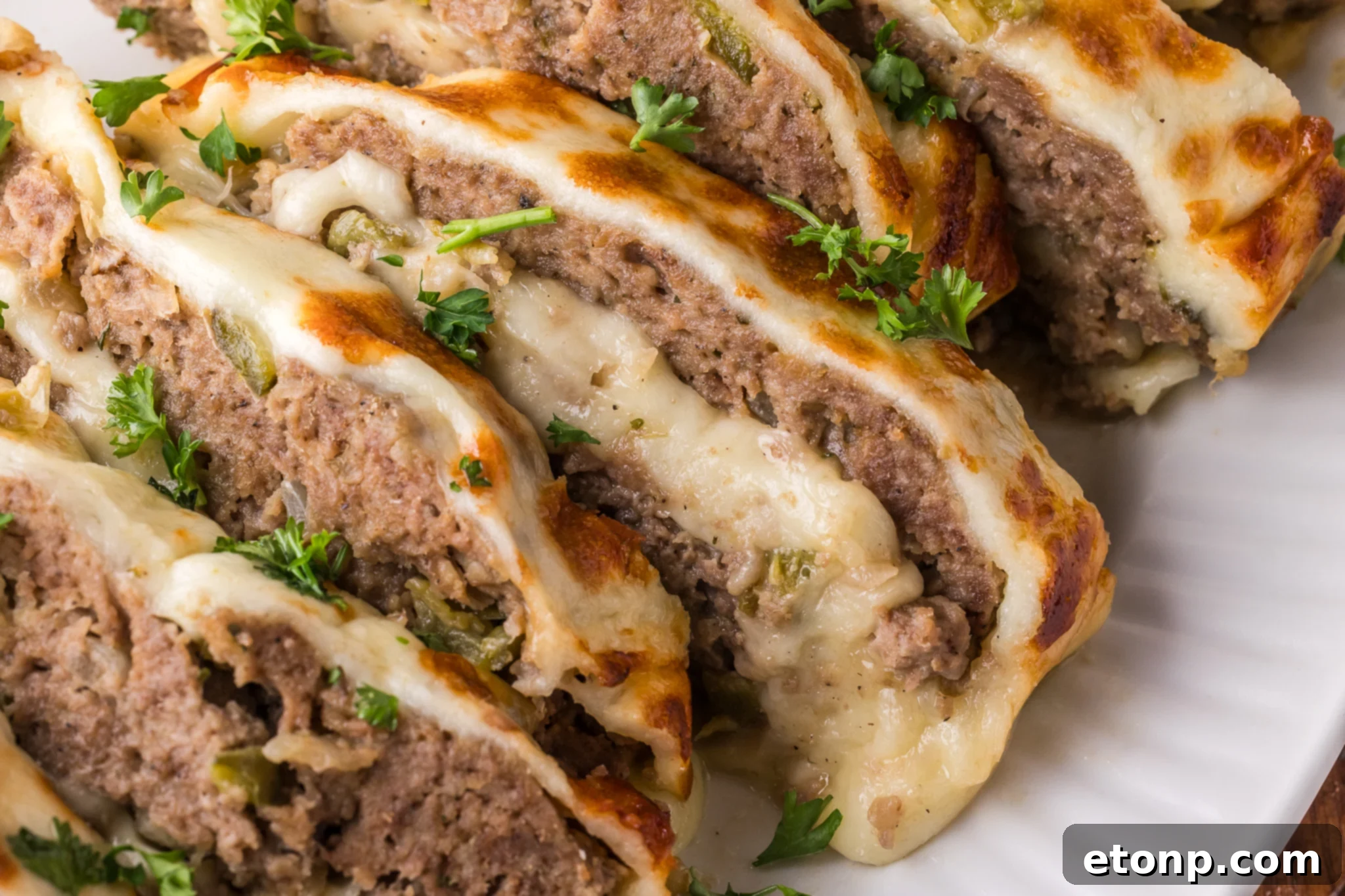 Cheesy Philly Stuffed Meatloaf with Peppers and Onions 24 zoomed in shot of the Philly Cheesesteak Meatloaf sliced on a white serving plate showing the inside with melty cheese