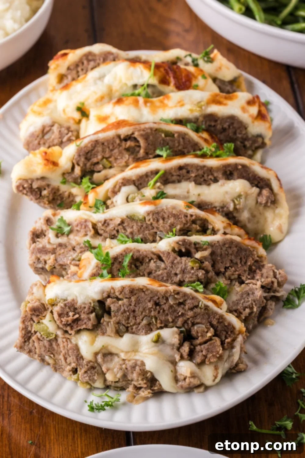 Cheesy Philly Stuffed Meatloaf with Peppers and Onions 4 large platter sitting on table that has sliced Stuffed Philly Cheesesteak Meatloaf on it, and other platters with food for serving up a meal for a family on wooden table