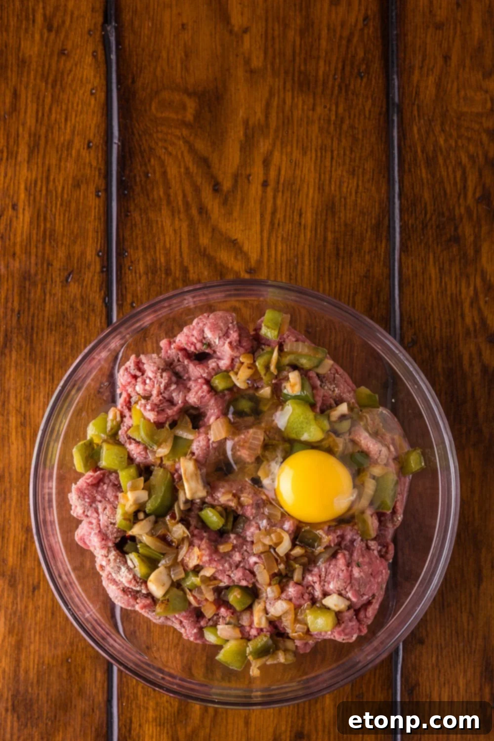 Cheesy Philly Stuffed Meatloaf with Peppers and Onions 7 raw meat, with egg, and onions and peppers on a glass bowl on a wooden table