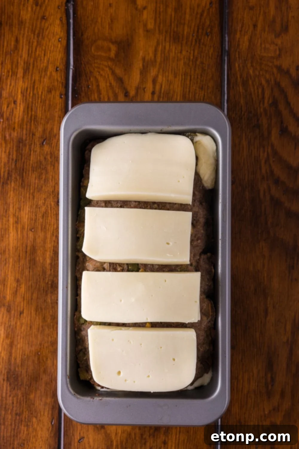 Cheesy Philly Stuffed Meatloaf with Peppers and Onions 10 slices of provolone sitting on top of a raw Stuffed Philly Cheesesteak Meatloaf in loaf pan