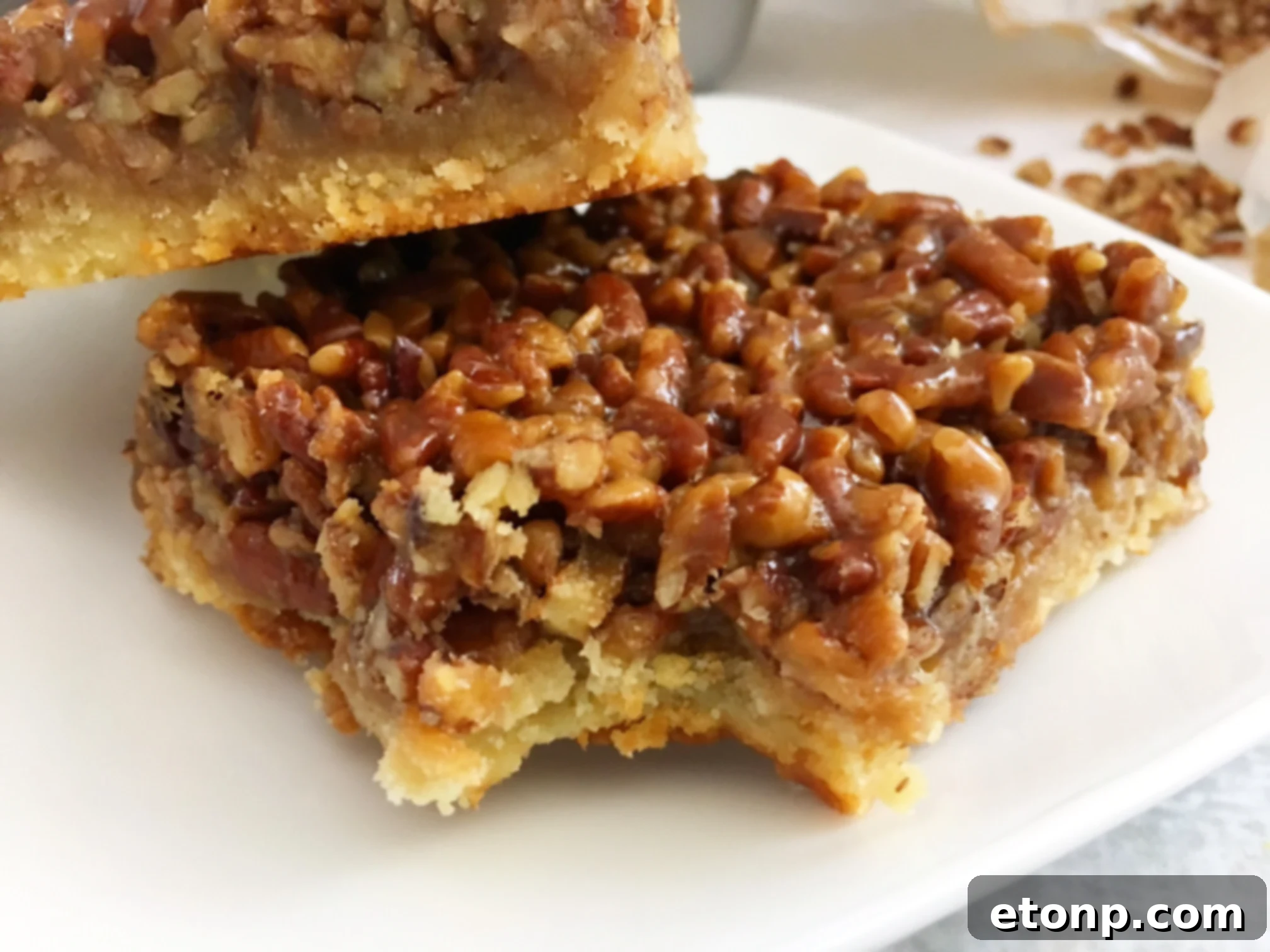 A close-up of a Pecan Pie Bar on a white plate, highlighting its rich texture and topping.
