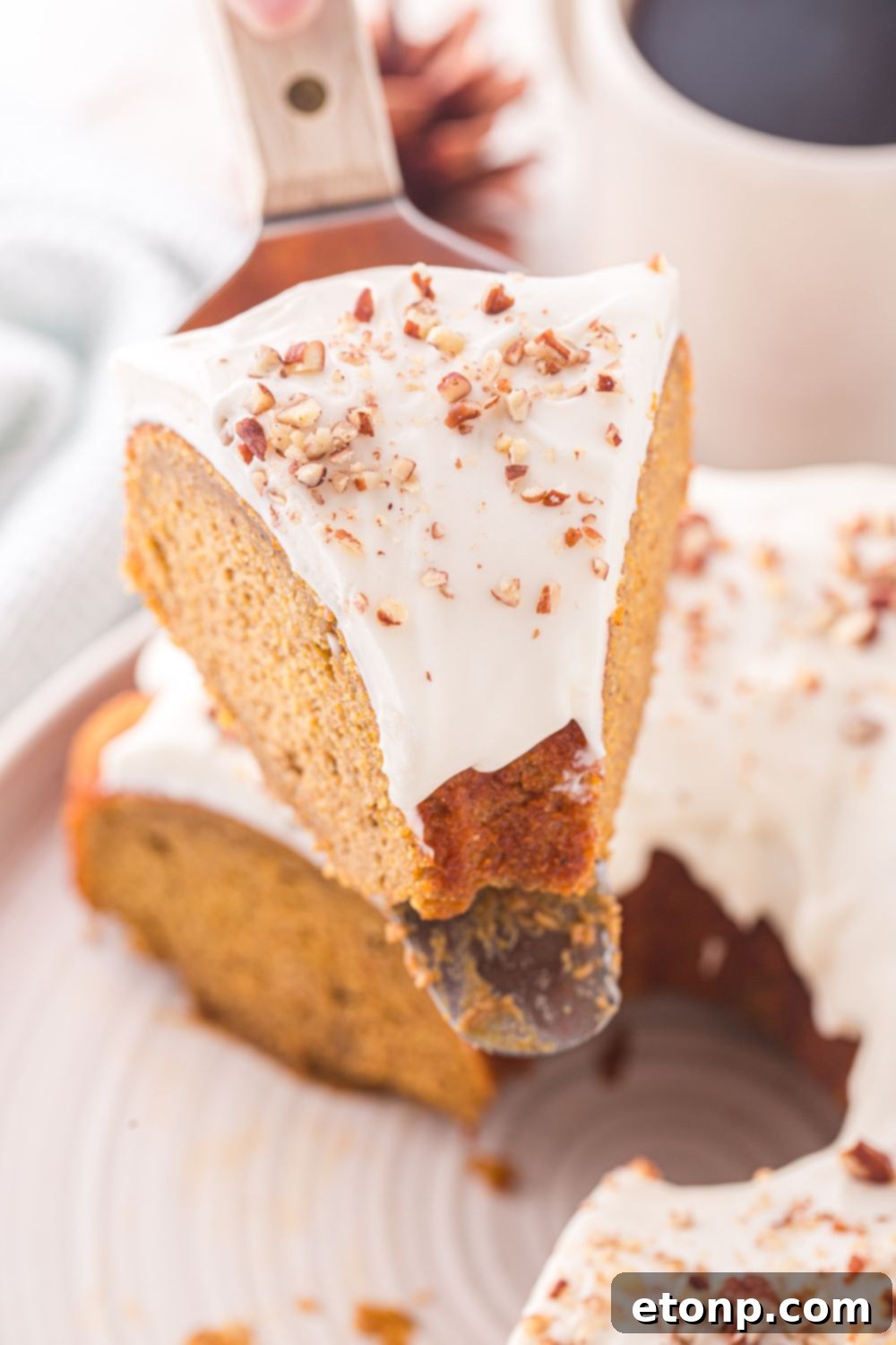 Pumpkin Bundt Cake on spatula above rest of cake on a white cake platter on table 