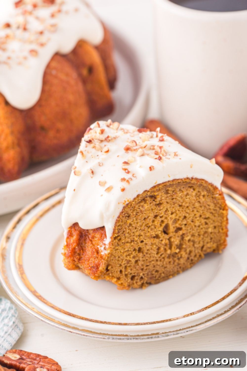 slice of Pumpkin Bundt Cake on a plate on the table with a glass of milk behind it and the rest of the cake to side 