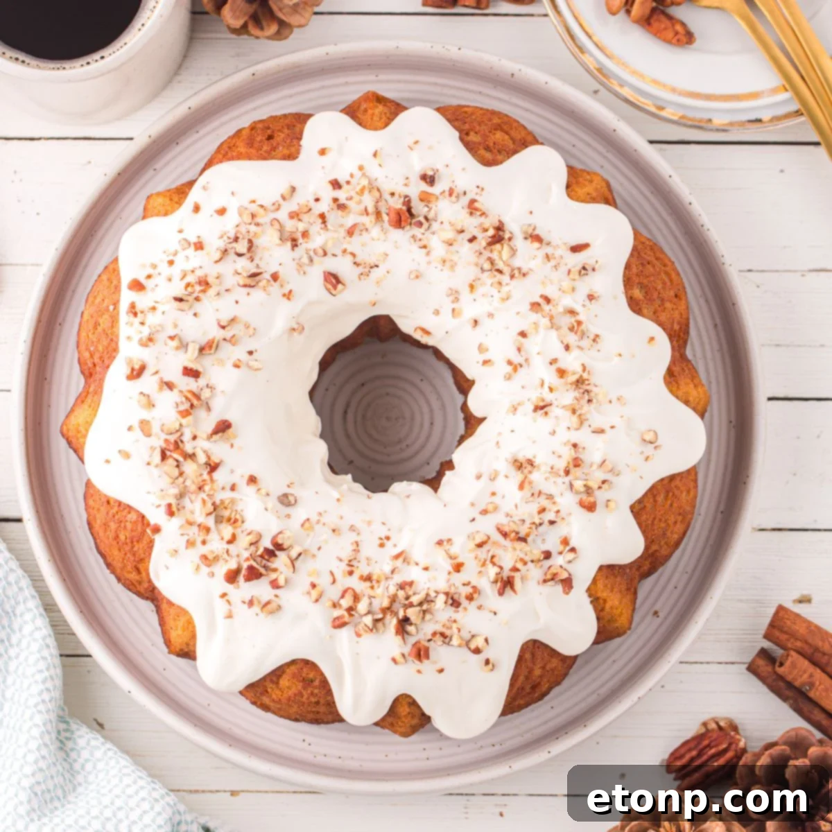 Pumpkin Bundt Cake with Cream Cheese Frosting sitting on a platter on a wooden table with cinnamon sticks and pine cone around it on table 
