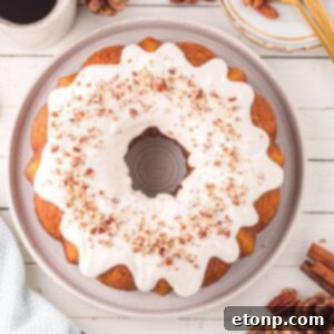 Pumpkin Bundt Cake with Cream Cheese Frosting sitting on a platter on a wooden table with cinnamon sticks and pine cone around it on table