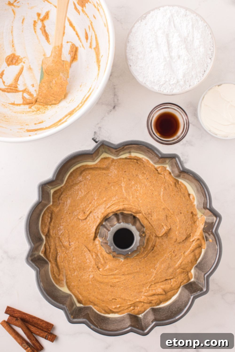 Pumpkin Bundt Cake patter in a bundt pan, with bowls around it full of ingredients for frosting 