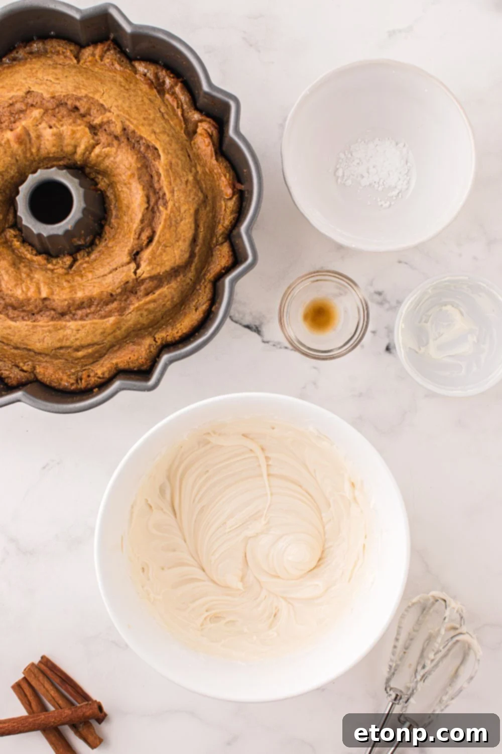 baked pumpkin bundt cake in pan with all the ingredients for cream cheese frosting in bowls around table 