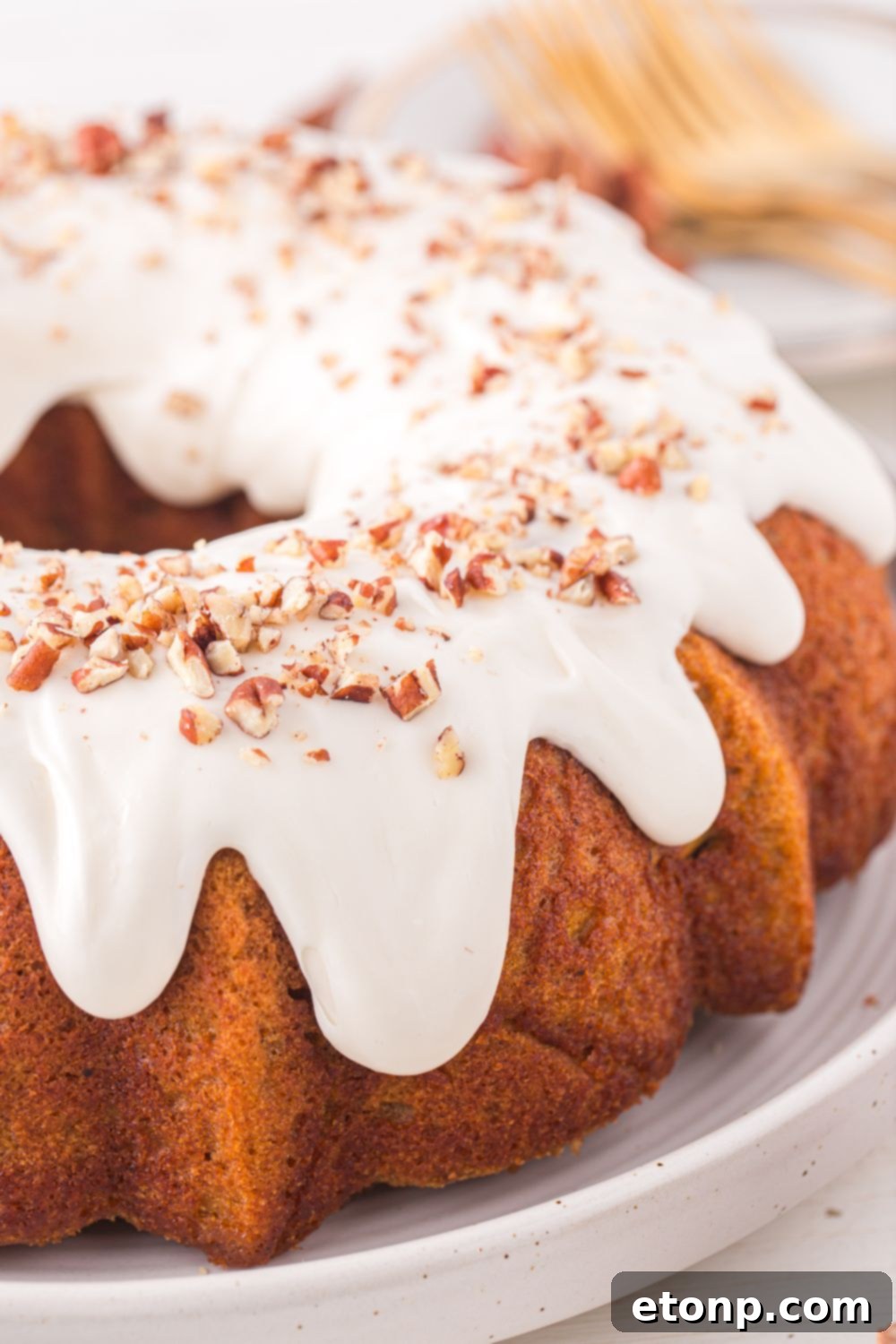 Pumpkin Bundt Cake on a white platter that is topped with cream cheese glaze and chopped nuts 