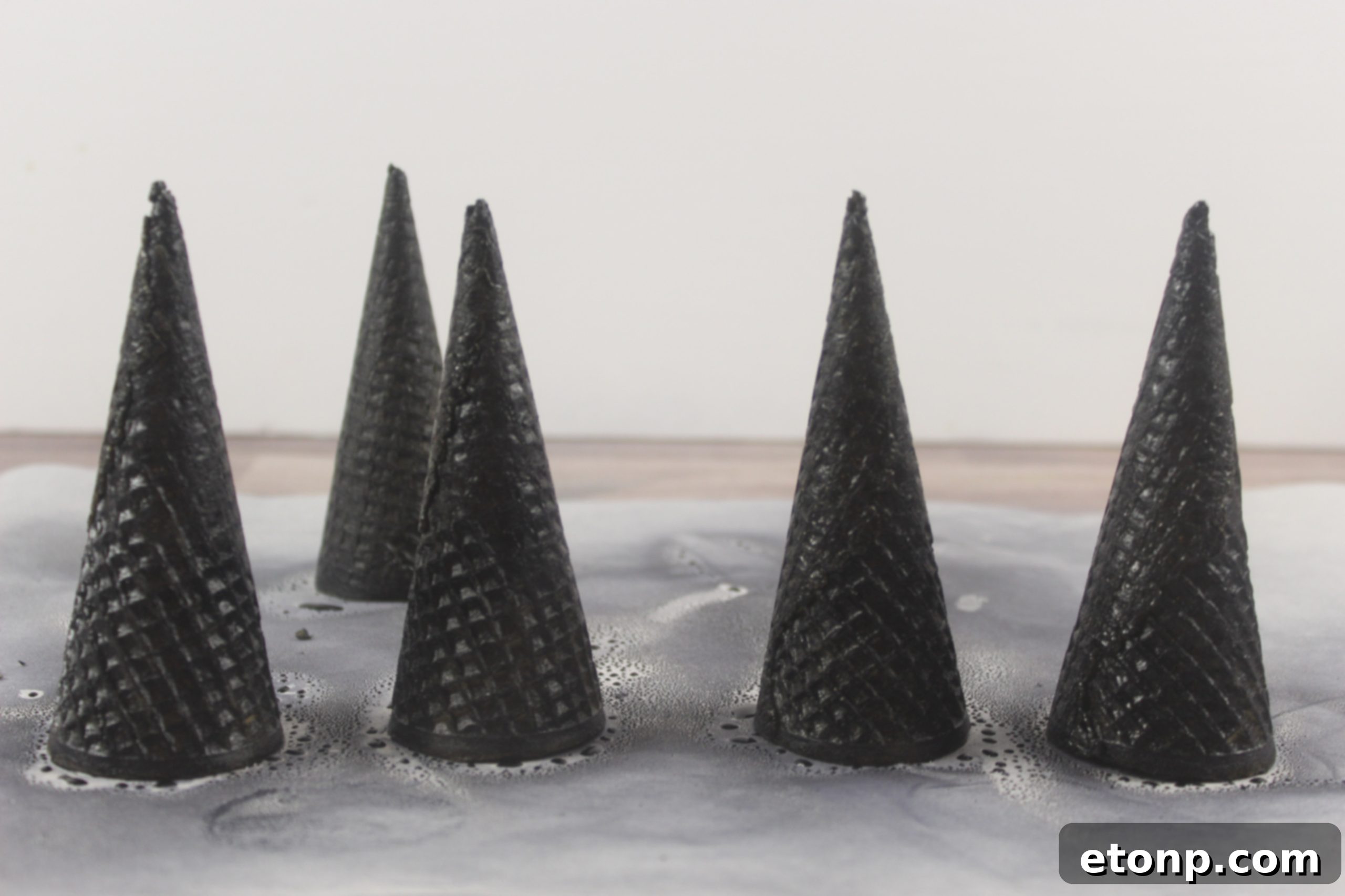 Applying edible black color mist spray to a sugar cone for a dark witch hat effect