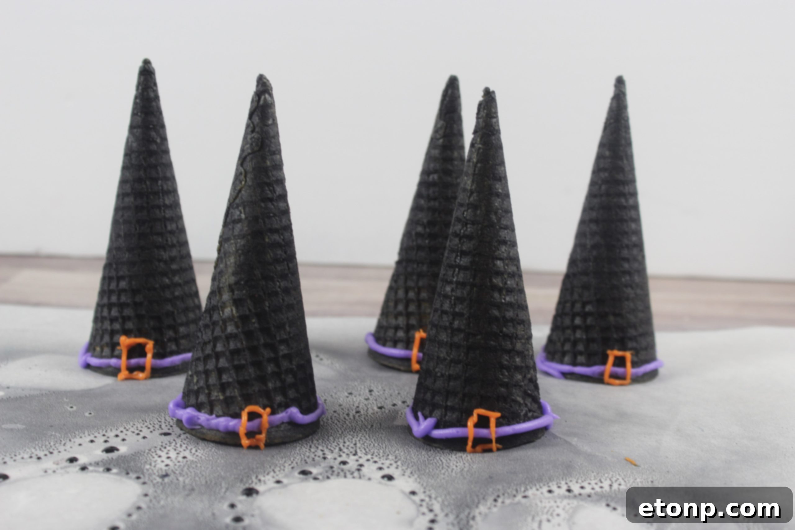 Decorating a black sugar cone witch hat with purple and orange icing for a buckle and rim