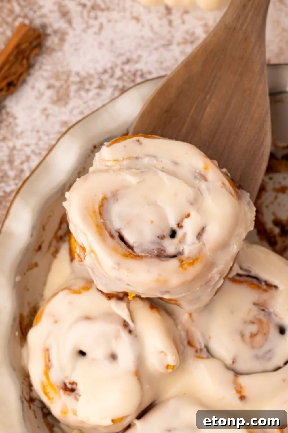 Effortless 2-Ingredient Pumpkin Cinnamon Rolls No Yeast 19 Pumpkin Cinnamon Rolls in a pie plate on table with a wooden spatula scooping one out of the pan