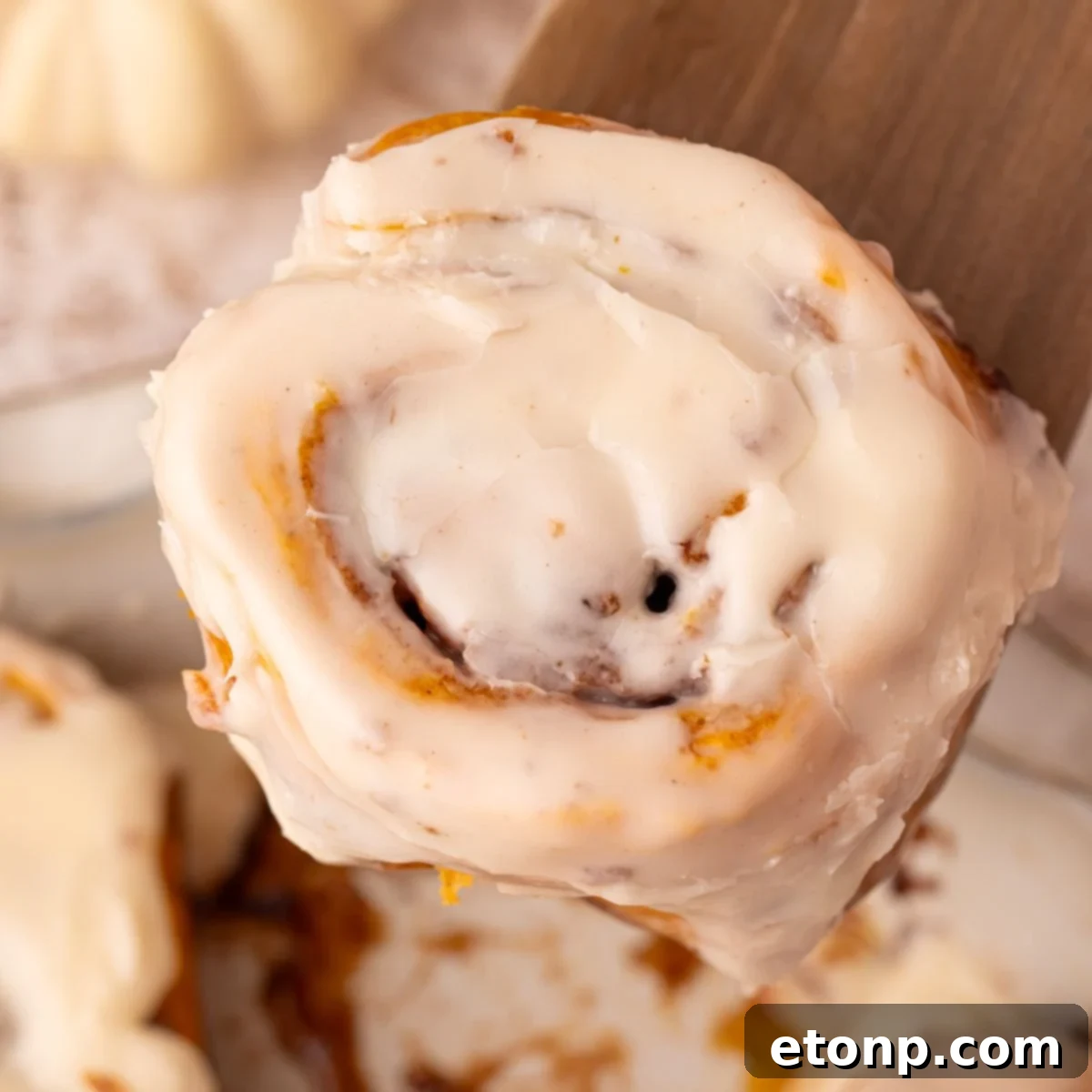 Effortless 2-Ingredient Pumpkin Cinnamon Rolls No Yeast 3 2 Ingredient Pumpkin Cinnamon Rolls in a pan sitting on table with one on a wooden spatula being lifted above the pan