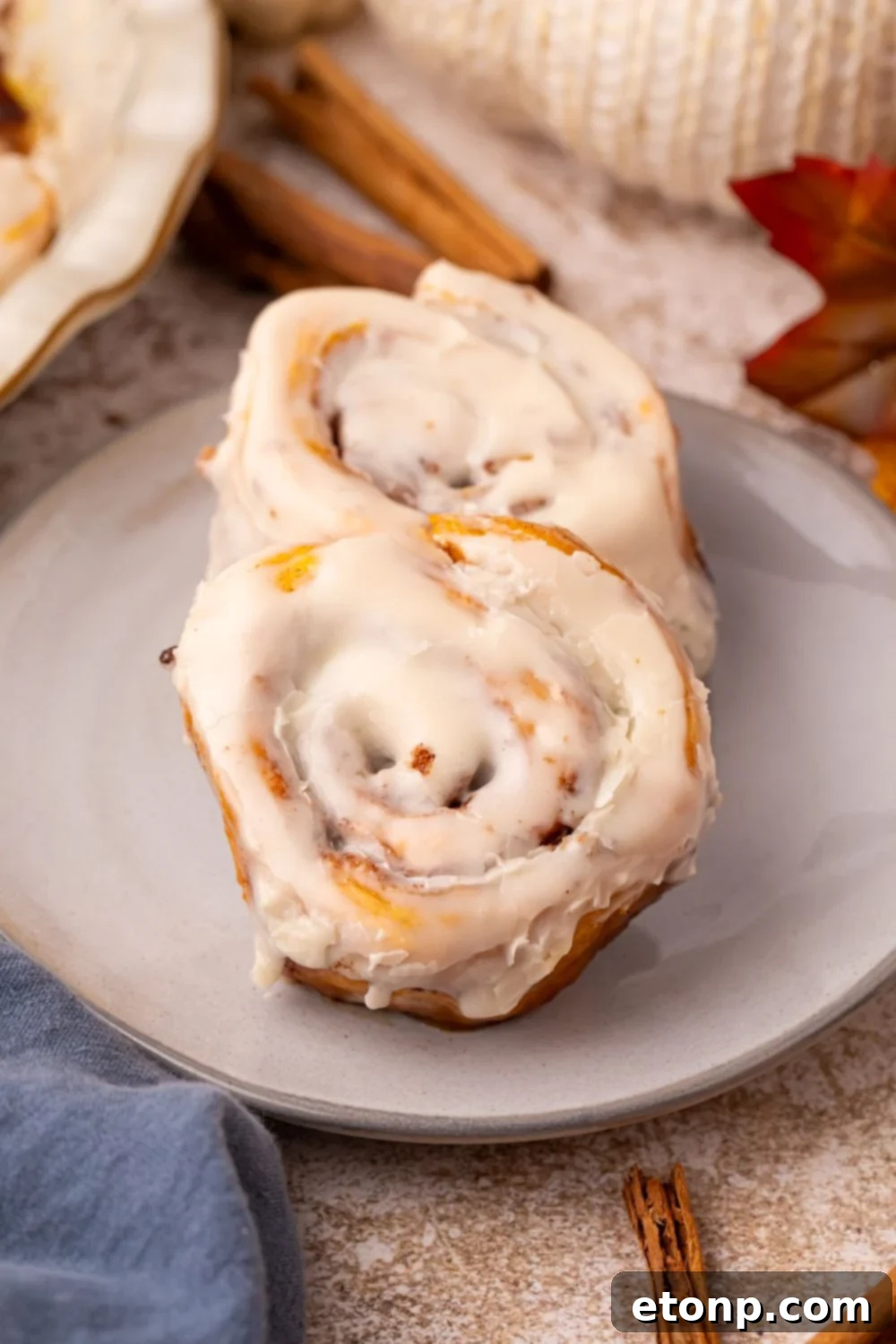 Effortless 2-Ingredient Pumpkin Cinnamon Rolls No Yeast 22 2 Pumpkin Cinnamon Rolls on a plate with cinnamon sticks, pumpkins and more fall themed items decorated around table